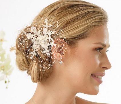 Eine Frau mit blondem Haar trägt ein weißes Spitzenhaarteil mit Diamantohrring und lächelt für ein Foto.