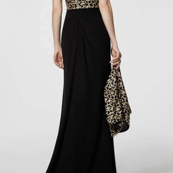 Eine Frau in einem schwarzen Abendkleid mit Leopardenmuster-Oberteil und passender Handtasche steht vor weißem Hintergrund.