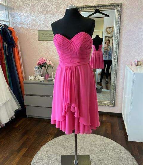 Ein rosa Brautjungfernkleid auf einem Mannequin, ausgestellt in einem Raum mit rosa Tapete und einem großen Spiegel.