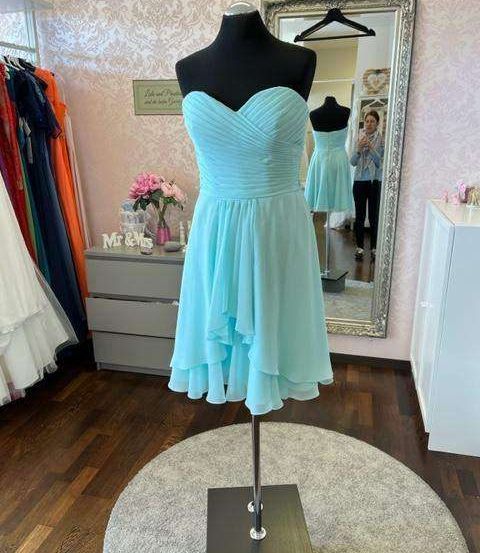 Ein Mannequin in einem mintgrünen Kleid wird in einem Boutique ausgestellt. Dahinter reflektiert ein Spiegel den Raum mit einem Schrank, Blumen und anderen Kleidern.