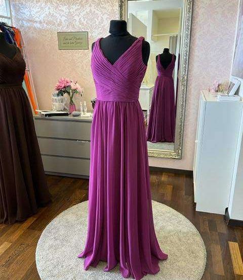 Ein lila Abendkleid wird auf einem Mannequin in einem Raum mit Holzboden und einem Spiegel ausgestellt.