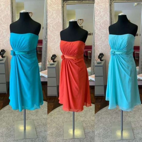 Drei Mannequins präsentieren Kleider in Türkis, Orange und einem weiteren Türkis. Sie stehen auf einem Teppichboden mit Spiegeln, die einen Raum reflektieren.