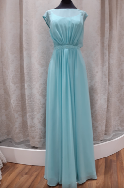 Ein Mannequin zeigt ein langes, hellblaues, ärmelloses Abendkleid mit enger Taille und fließendem Rock vor einem Hintergrund weißer Vorhänge.