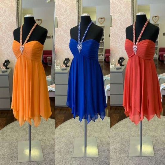 Drei Mannequins in einem Raum, jedes mit einem anderen Farbton eines bestickten Kleides: orange, blau und rot. Die Kleider haben schulterfreie Designs. Der Hintergrund besteht aus einem Spiegel und einer pink gemusterten Wand.