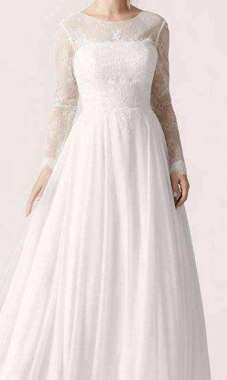 Eine Frau in einem weißen Hochzeitskleid mit Spitzenärmeln und einem langen Rock posiert für ein Foto.