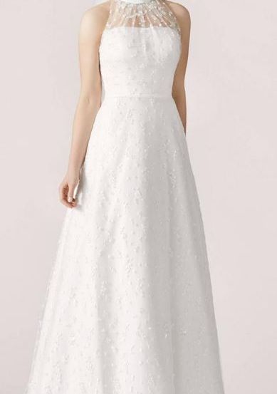 Eine Frau in einem weißen Hochzeitskleid mit hohem Kragen und Blumendesign posiert für ein Foto. Sie trägt auch einen Schleier.