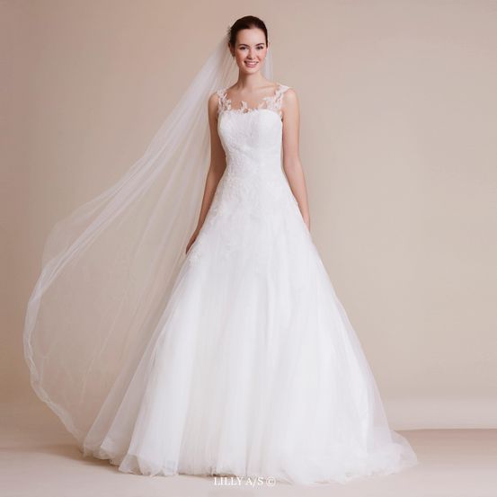 Eine Frau posiert für ein Foto in einem weißen Hochzeitskleid und Schleier. Sie lächelt und schaut in die Kamera.