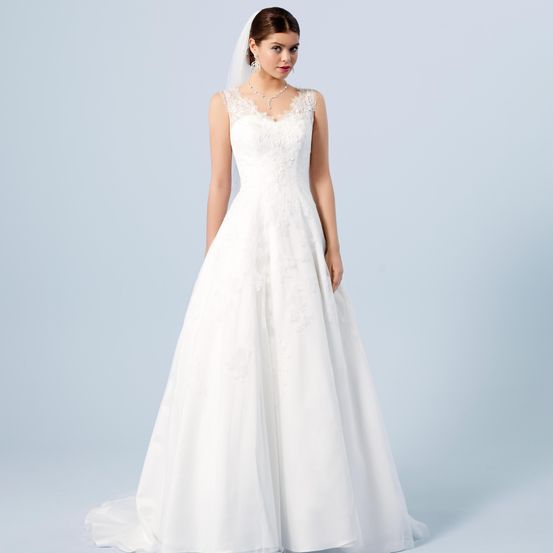 Eine Frau in einem weißen Hochzeitskleid steht vor einem blauen Hintergrund, trägt einen Schleier und eine Halskette.