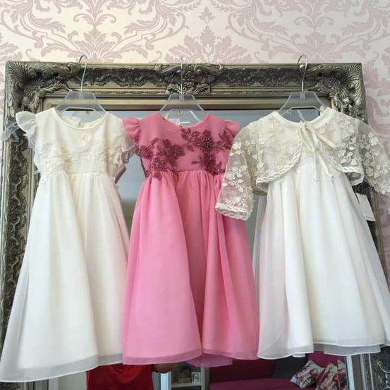 Drei Kleider hängen vor einem Spiegel vor einer rosa Tapete. Ein weißes, ein rosa und ein weißes Kleid mit Spitze.