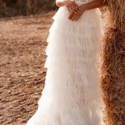 Eine Braut in einem weißen Kleid steht neben einem Heuballen in einer ländlichen Umgebung, ihre Hände ruhen auf ihrer Taille.