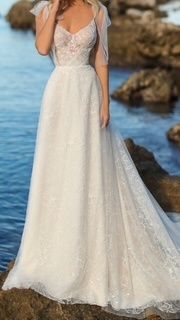 Eine Frau in einem Hochzeitskleid steht auf einem felsigen Ufer am Meer und blickt auf das Wasser.