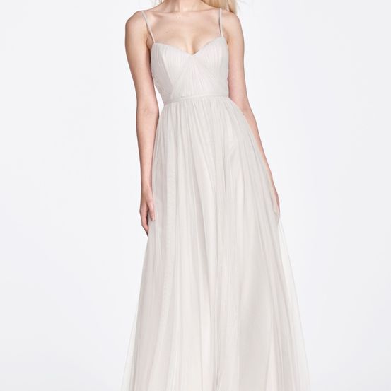 Eine Frau trägt ein helles, ärmelloses, langes, fließendes Kleid mit V-Ausschnitt und enger Taille.