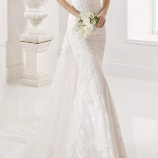 Eine Braut steht in einem eleganten weißen Hochzeitskleid, hält einen Strauß weißer Blumen und hat eine dekorative Urne im Hintergrund.