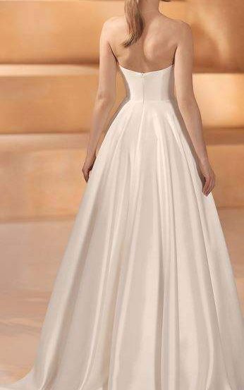 Eine Frau in einem trägerlosen weißen Satin-Hochzeitskleid mit hohem Rücken und vollem Rock, die auf einer Holztreppe steht.