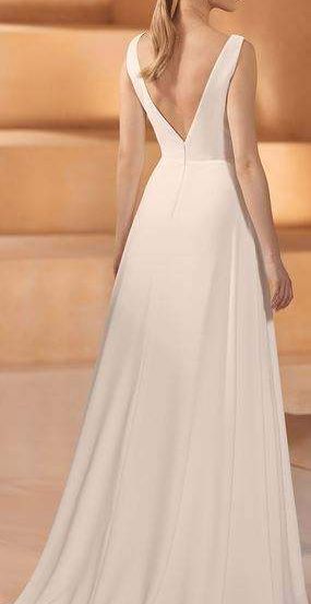 Eine Frau in einem weißen Kleid mit V-Ausschnitt und fließendem Rock steht auf einer hölzernen Treppe.