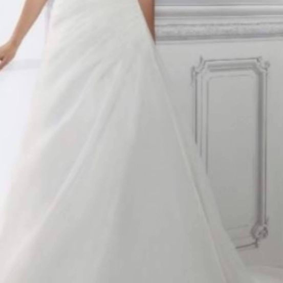 Eine Person steht in einem weißen Kleid vor einer weißen Wand mit dekorativen Mustern.