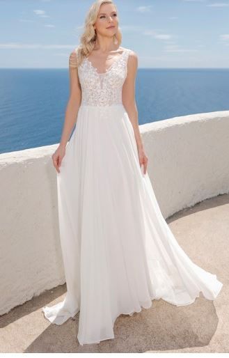 Eine Frau mit blonden Haaren in einem weißen Kleid steht auf einem Balkon mit Blick auf das Meer.