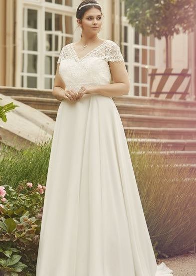 Eine Frau in einem weißen Hochzeitskleid steht vor einem Gebäude mit Treppen und Fenstern.