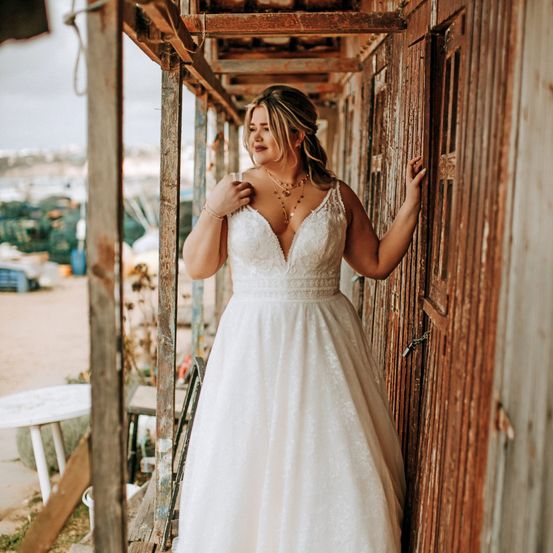 Eine Frau in einem weißen Hochzeitskleid steht in einer alten Holzstruktur, möglicherweise für ein Foto.
