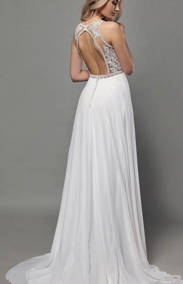 Eine Frau in einem weißen, bodenlangen Hochzeitskleid mit einem verzierten Spitzenrücken und einer besetzen Taillenband, die vor einem grauen Hintergrund steht.