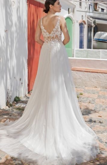 Eine Frau steht draußen mit dem Rücken gekehrt, trägt ein weißes Hochzeitskleid mit Spitzendetails, in der Nähe einer roten Tür.