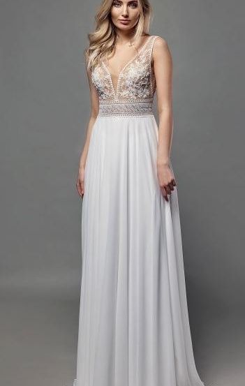 Eine Frau trägt ein weißes Abendkleid mit aufwendigen Spitzendetails am Oberteil, vor einem grauen Hintergrund.