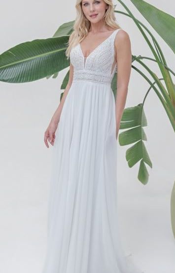 Eine Frau steht vor einer Pflanze mit großen grünen Blättern und trägt ein weißes, ärmelloses Hochzeitskleid mit V-Ausschnitt.