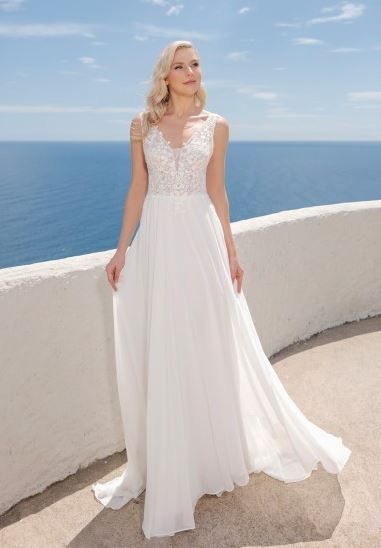 Eine Braut in einem weißen Kleid steht auf einem Balkon mit Blick auf den Ozean. Der Himmel ist blau mit einigen Wolken.