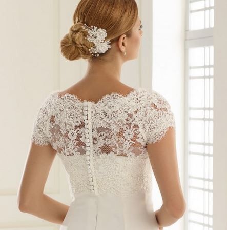 Eine Frau mit einer Hochzeitsfrisur und einem Spitzenhochzeitskleid schaut zurück, ihr Haar geschmückt mit einer weißen Blume.