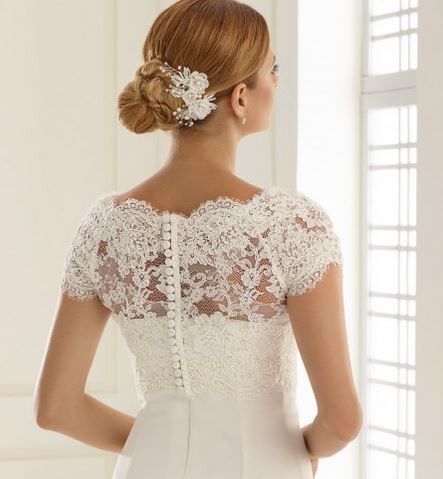 Eine Frau mit einer Hochzeitsfrisur und einem Spitzenhochzeitskleid schaut zurück, ihr Haar geschmückt mit einer weißen Blume.