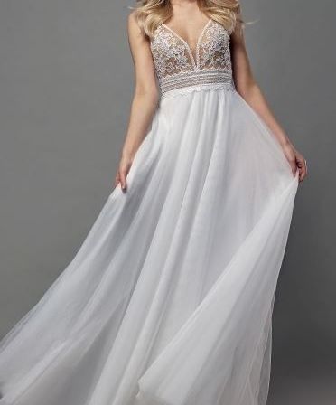 Eine Frau mit blondem Haar trägt ein weißes Spitzenhochzeitskleid und rote Sandalen und posiert für ein Foto.