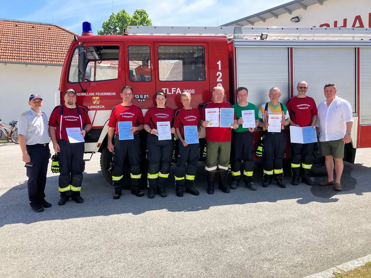 Eine Gruppe von Feuerwehrleuten in Uniform steht vor einem Feuerwehrwagen. Sie halten Urkunden und posieren für ein Foto.