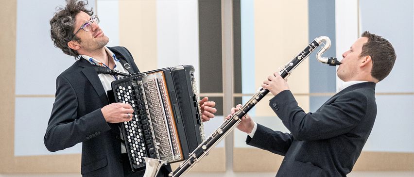 Zwei Musiker spielen, einer spielt Akkordeon und der andere Klarinette, nebeneinander stehend.