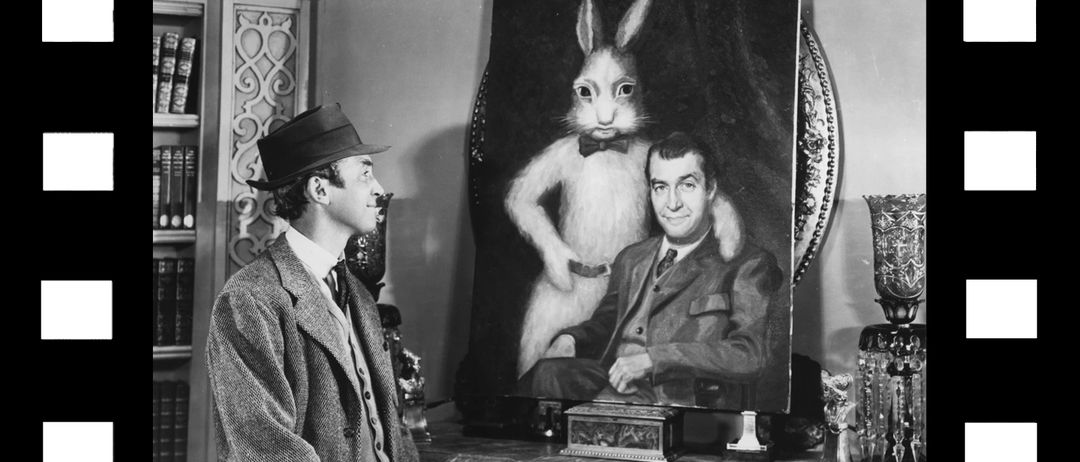 Ein Schwarz-Weiß-Foto eines Mannes in einem Anzug, der ein großes Gemälde eines Kaninchens mit einer Fliege betrachtet.