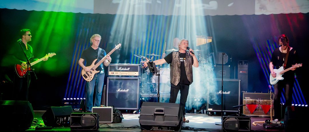 Eine Band tritt auf der Bühne mit Marshall-Verstärkern auf, ein Mann singt in ein Mikrofon und ein anderer spielt Gitarre.