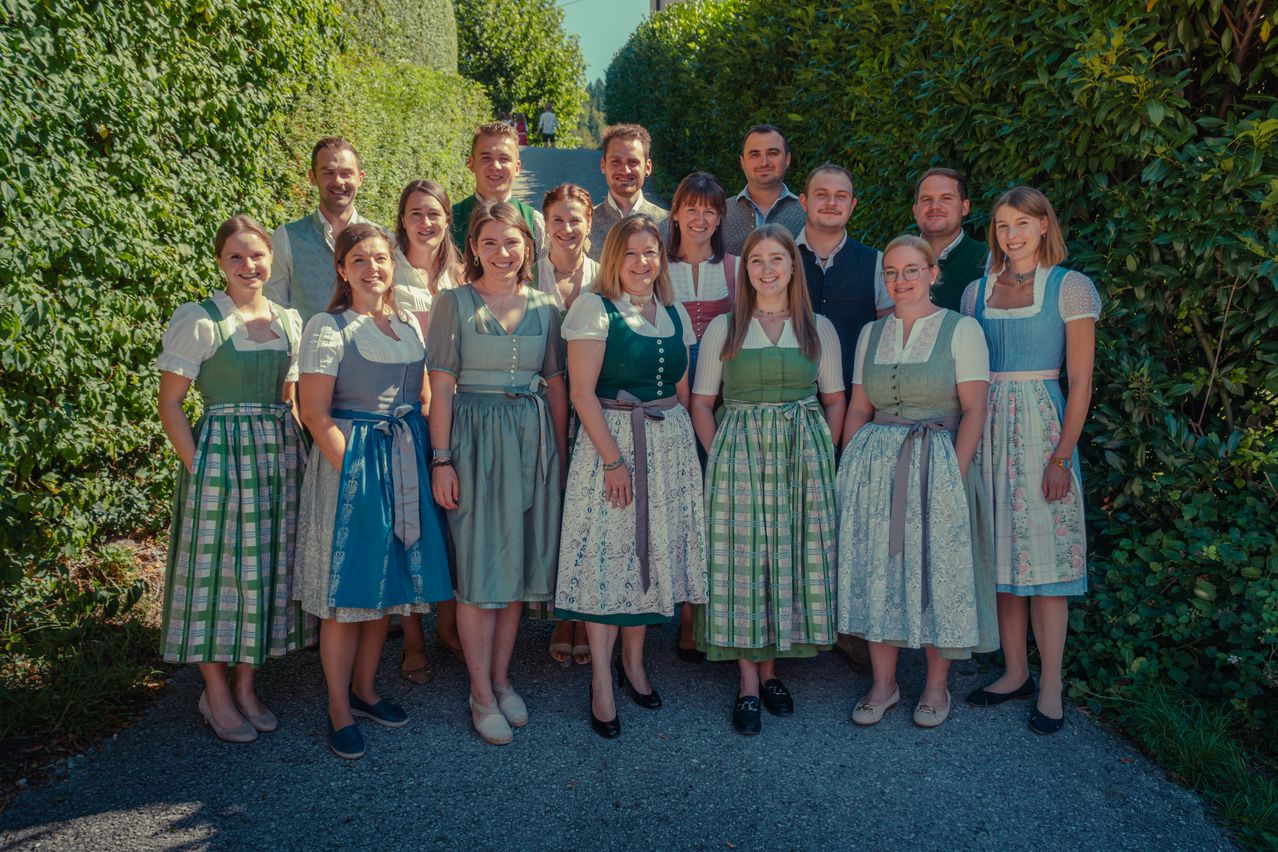 A group of people dressed in traditional clothing, smiling and posing for a photo in a garden.