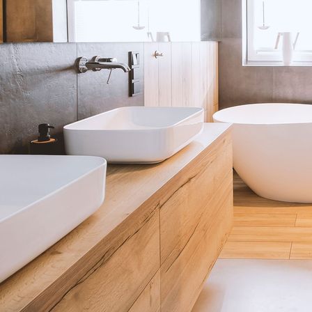Ein modernes Badezimmer mit Badewanne, doppelten Waschbecken, Holzboden und einem Spiegel an der Wand.