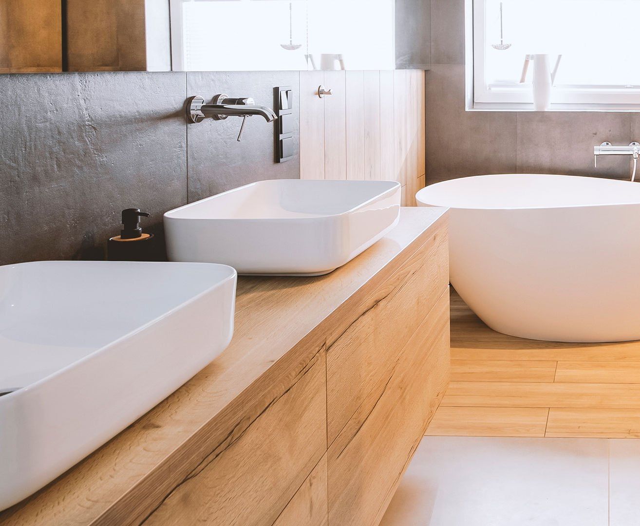 Ein modernes Badezimmer mit Badewanne, doppelten Waschbecken, Holzboden und einem Spiegel an der Wand.
