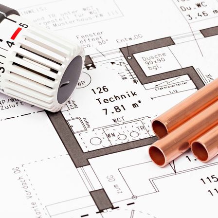 Ein weißer Thermostat liegt auf einem technischen Plan mit Kupferrohren. Er hat die Aufschrift '5' und '126 Technik' darauf. Der Plan hat Maße und ein Diagramm.