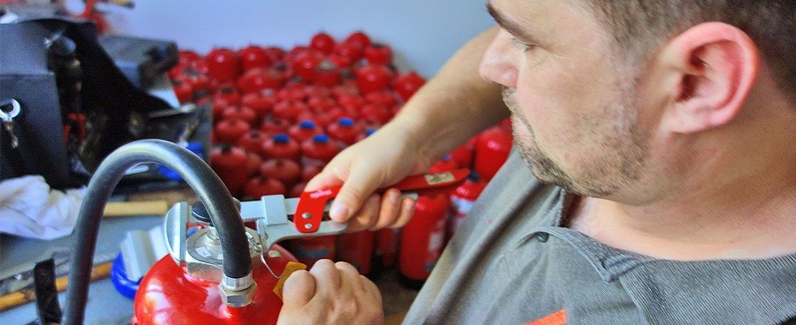 Ein Mann hält einen Feuerlöscher und untersucht ihn in einem Lager oder einer Lagerhalle.