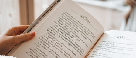 Eine Hand hält ein offenes Buch mit dem Titel 'Vorlesen in der Bibliothek'. Die Seiten des Buches zeigen deutschen Text. Darunter sind die Texte 'Datum: jeden Donnerstag' und 'Uhrzeit: ab 16:30 Uhr' sichtbar. Zusätzlicher Text lautet 'Erlebt jeden Donnerstag Vorlesezeit mit Daniela bei uns in der Bibliothek Schins'.