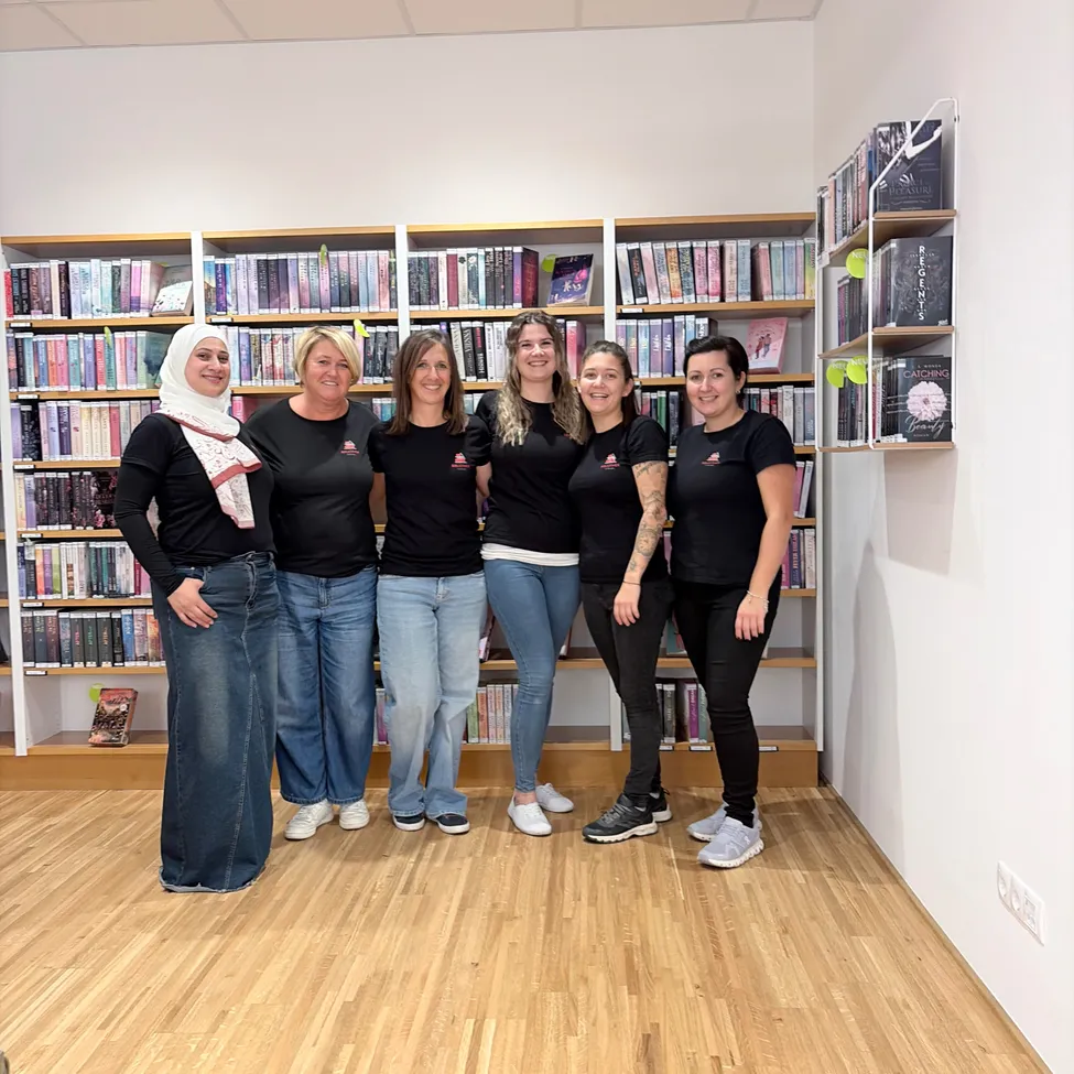 Eine Gruppe von Frauen in schwarzen T-Shirts steht vor einem Bücherregal in einem Raum.