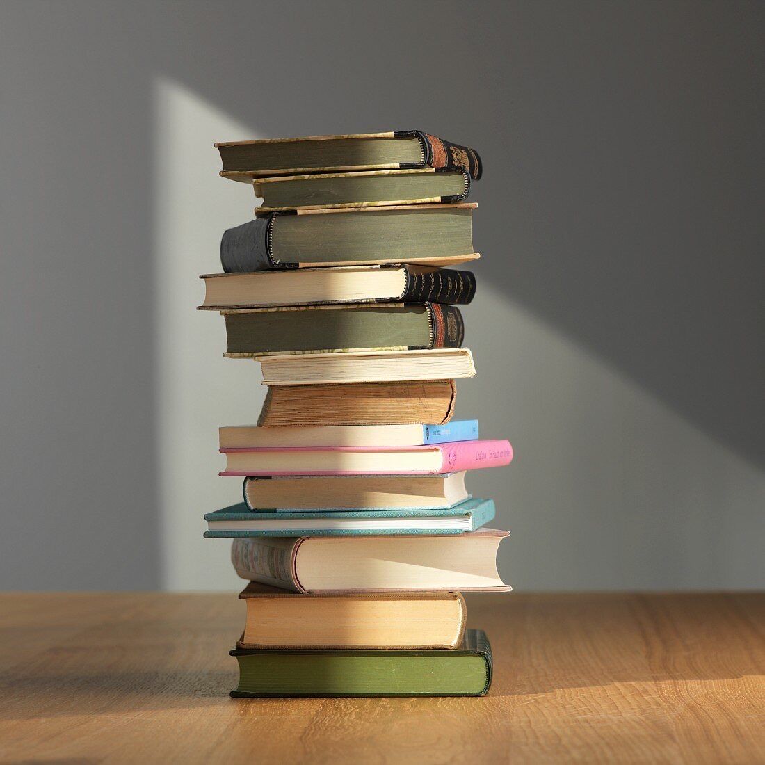 Ein Stapel Bücher mit verschiedenen Farben und Größen auf einem Holztisch vor einer grauen Wand.