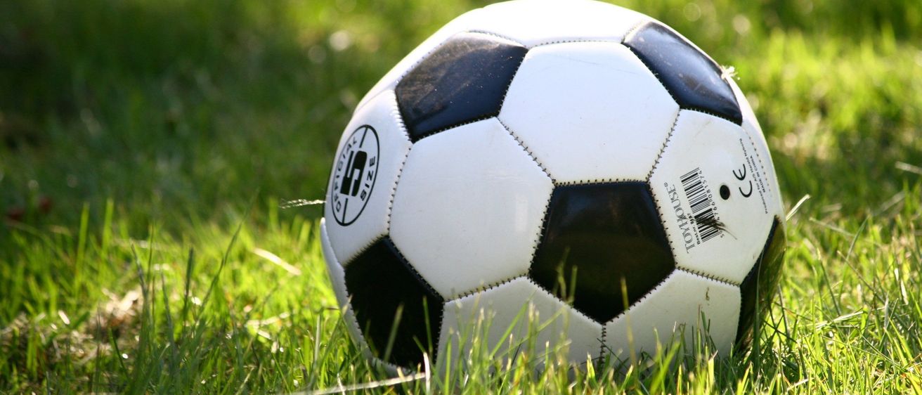 Ein weißer und schwarzer Fußball, Größe 4, liegt auf einem Rasenfeld im Sonnenlicht.