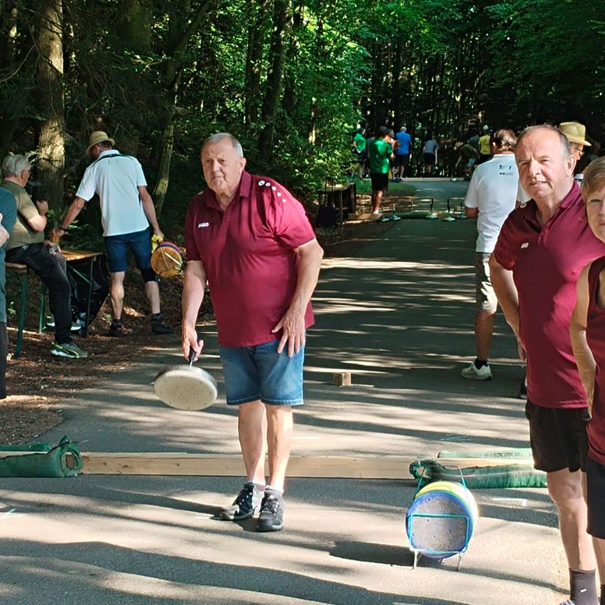 Menschen spielen Boule im Park. Ein Mann wirft einen Ball auf das Ziel. Andere schauen zu.