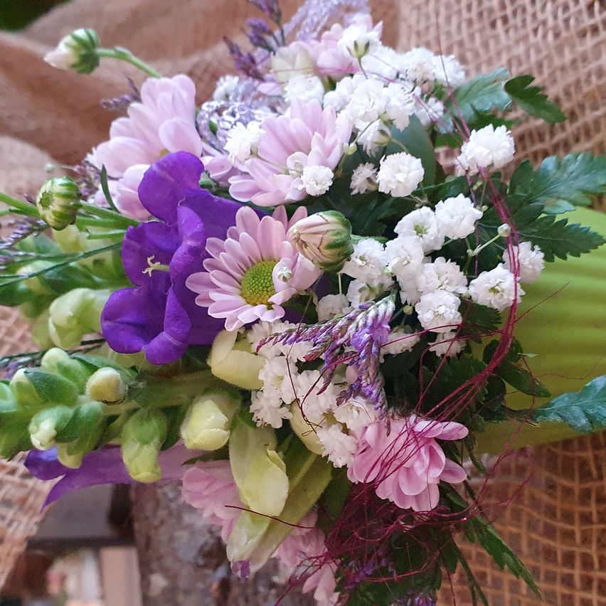 Ein Nahaufnahme eines Straußes aus verschiedenen Blumen in Rosa-, Lila- und Weißtönen mit grünen Blättern, in einer natürlichen Umgebung arrangiert.