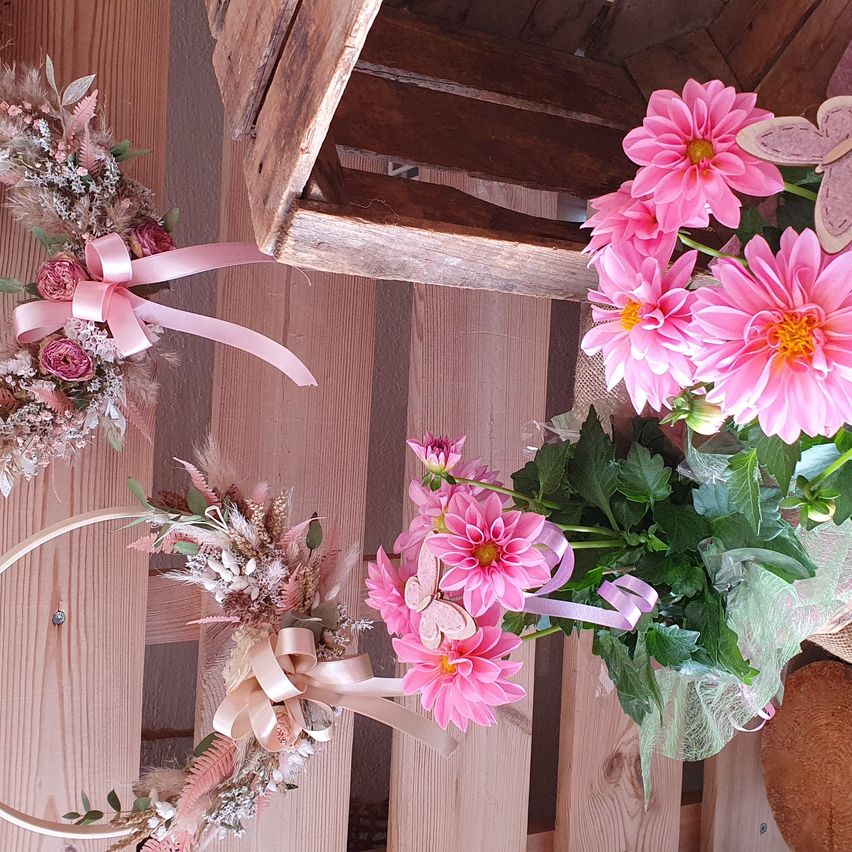 Ein pinkfarbenes Blumenarrangement mit einem Schmetterling und einer Schleife auf einer Holzoberfläche. Die Blumen sind in einem Strauß mit einem Schmetterling in der Mitte.