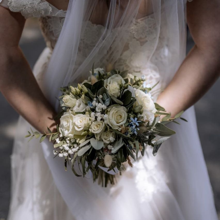 Eine Braut in einem weißen Hochzeitskleid und Schleier hält einen Strauß weißer Rosen und Grün.