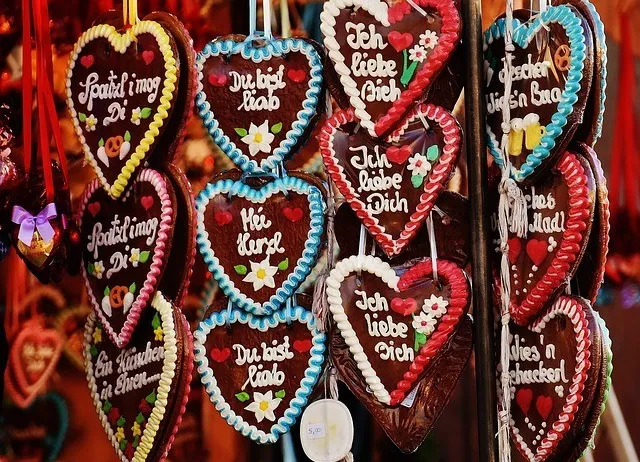 Eine Vielzahl von herzförmigen Schokoladen hängt an einem Ständer. Jede Schokolade hat einzigartige Designs und Texte, einschließlich Phrasen wie 'Ich liebe dich' und 'Du bist wunderbar.' Die Schokoladen haben ein festliches Aussehen und deuten darauf hin, dass sie für einen besonderen Anlass bestimmt sind.