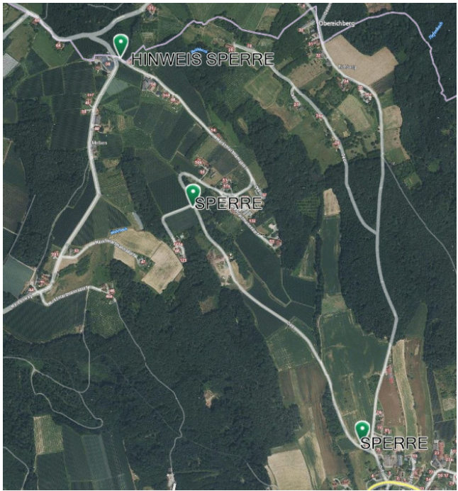 Luftaufnahme eines ländlichen Gebiets mit grünen Feldern, kleinen Straßen und Häusern. Das Gebiet heißt Sperre. Es gibt grüne Markierungen, die bestimmte Orte anzeigen.